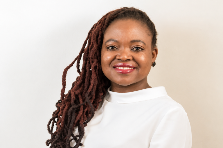 How Sue Nyathi’s Netflix Breakthrough Brought Her Books to a Global Audience Zimbabwean author Sue Nyathi smiling in a white top, with her locs over one shoulder.